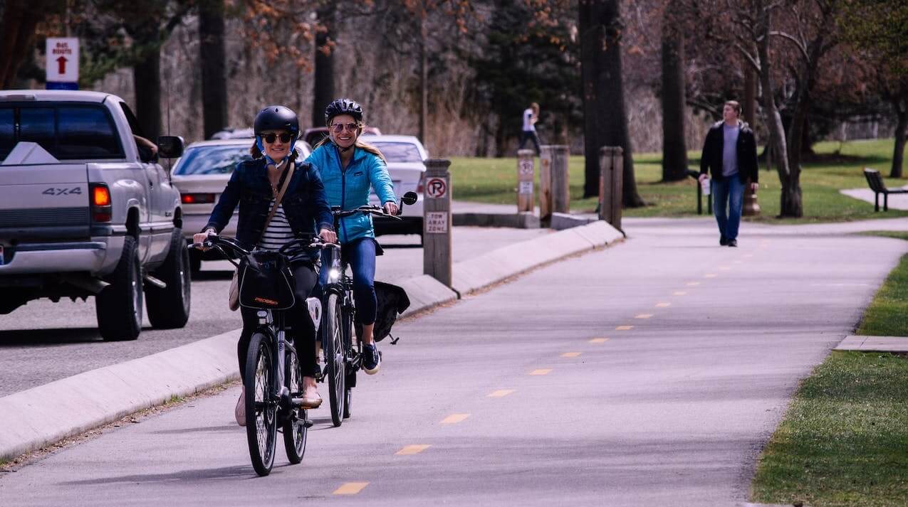 Dwie uśmiechnięte kobiety jadą ścieżką rowerową w mieście